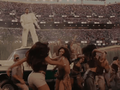 People Dancing In Stadium With Man In White Suit On Car GIF