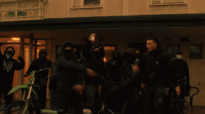 People In Front Of Building With Mask Saying A GIF