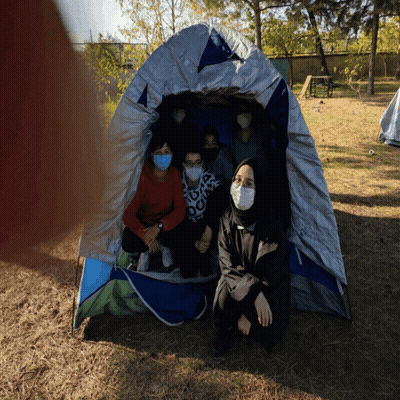 People In Masks Sitting In Tent GIF