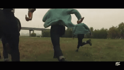 People Running Through Grassy Field In Front Of Bridge GIF