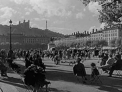 People Sitting At Tables In Park With Castle GIF