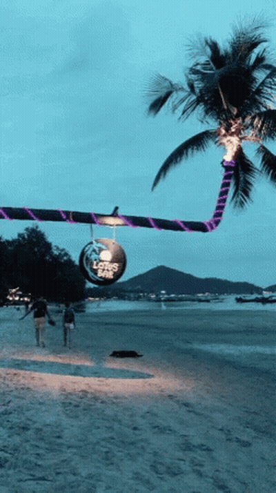 People Walking On A Beach With A Sign That Says Lotus Cafe GIF
