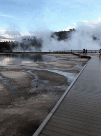 People Walking On A Boardwalk Overlooking A Body Of Water With Steam Coming Out Of It GIF
