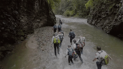 People Walking Through River With Backpacks GIF