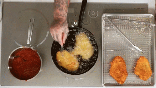 Person Frying Chicken In Frying Pan With Sauce Behind GIF