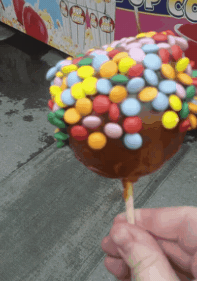 Person Holding Caramel Apple Covered In Colorful Candy GIF