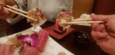 Person Holding Chopsticks Over Sushi GIF