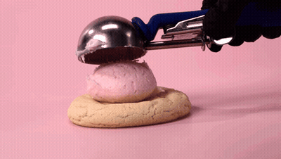 Person Holding Cookie With Pink Frosting GIF