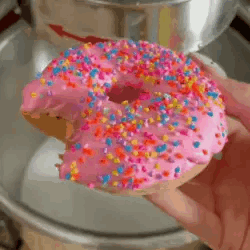 Person Holding Donut With Pink Frosting And Sprinkles GIF