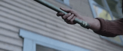 Person Holding Green Pipe in Front of Wooden House