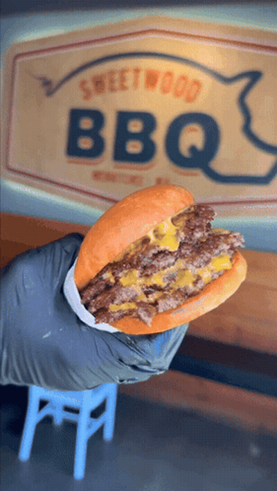 Person Holding Hamburger In Front Of BBQ Sign GIF