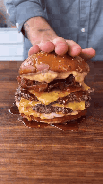 Person Holding Large Hamburger On Cutting Board GIF