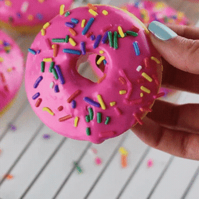Person Holding Pink Frosted Donut With Sprinkles GIF