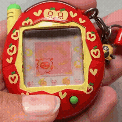 Person Holding Red And Yellow Tamagotchi With Hearts GIF