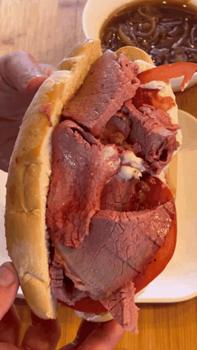 Person Holding Roast Beef Sandwich With Tomatoes And Onions GIF