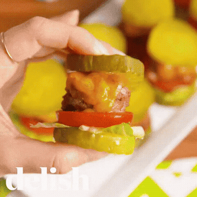 Person Holding Small Hamburger With Pickles and Cheese