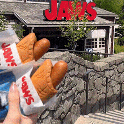 Person Holding Two Hot Dogs In Front Of Jaws Sign GIF
