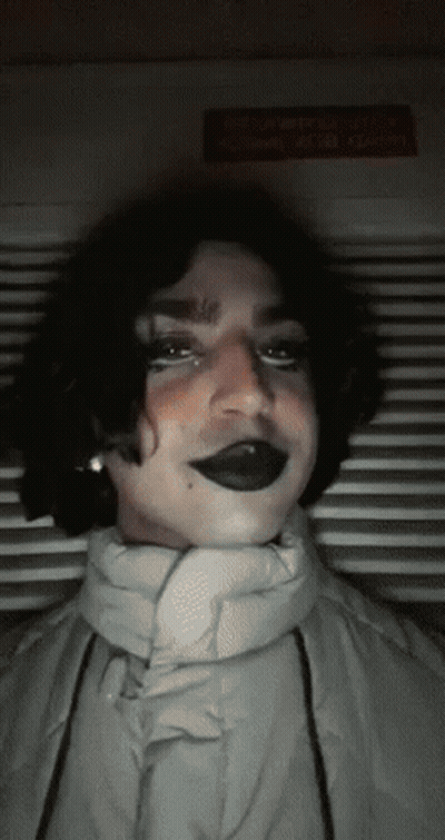 Person In Black Lipstick And White Jacket Looking At Camera GIF