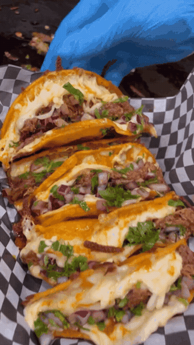 Person In Blue Gloves Holding Tray Of Tacos On Checkered Paper GIF