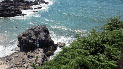 Person In Blue Shirt Standing On Rock Near Water GIF