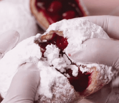 Person In Gloves Holding Pastry With Powdered Sugar And Cherry Filling GIF