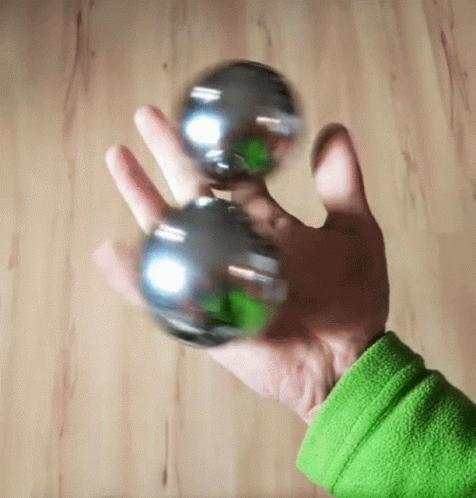 Person In Green Sweater Holding Two Silver Balls GIF