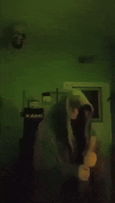 Person In Hoodie Standing In Dark Room With Green Background GIF