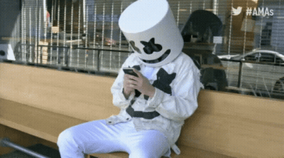 Person In Marshmallow Mask On Bench Looking At Phone GIF