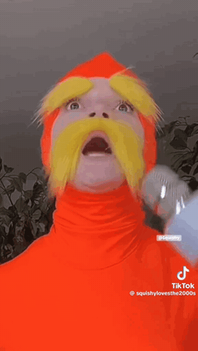 Person In Orange Costume With Yellow Mustache Holding Microphone GIF
