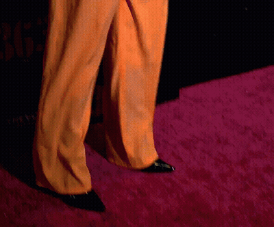 Person In Orange Pants And Black Shoes Walking On Pink Carpet GIF