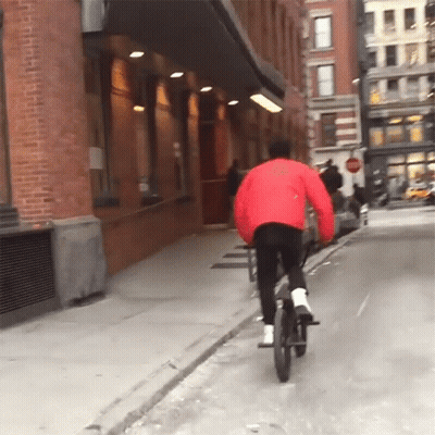 Person In Red Jacket Riding Bike Down Street GIF