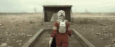Person In Red Jumpsuit And White Helmet Walking Through Desert GIF