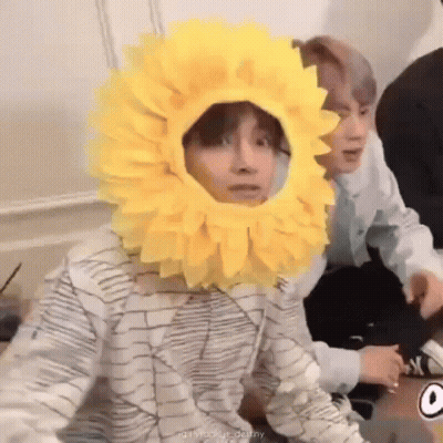 Person In Sunflower Hat Sitting Next To Another GIF
