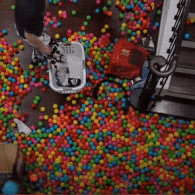 Person Laying In Pool Of Colorful Balls With Staircase GIF