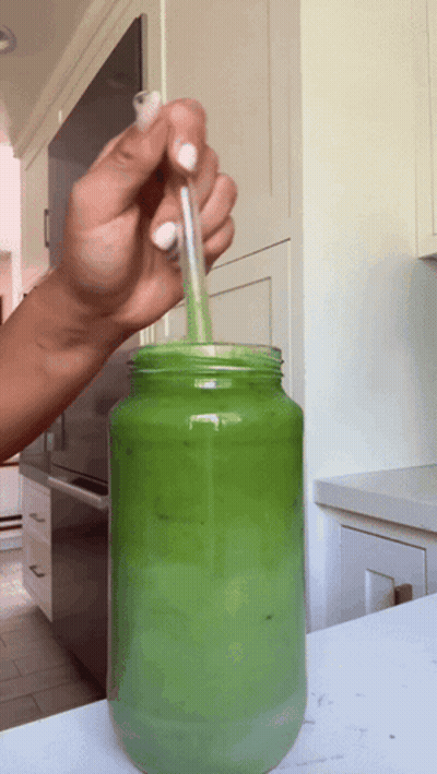 Person Pouring Green Liquid In Mason Jar With Straw GIF