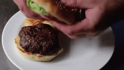 Person Putting Hamburger On Bun On Plate GIF