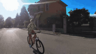 Person Riding Bike Down Street In Front Of Building GIF
