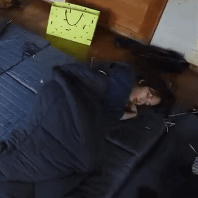 Person Sleeping In Sleeping Bag On Bed Next To Yellow Bag GIF