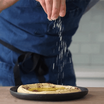 Person Sprinkling Salt On Hummus GIF