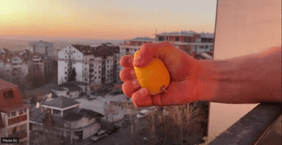 Person Squeezing Orange With City Pause (N) GIF