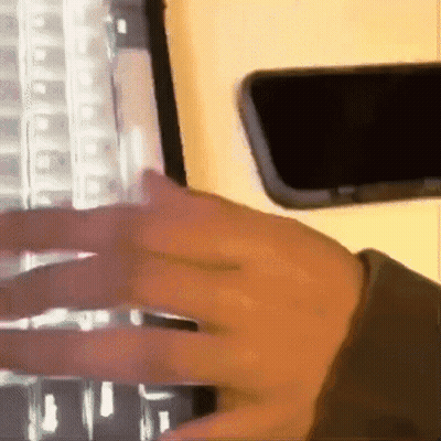 Person Typing On Keyboard Next To Phone GIF