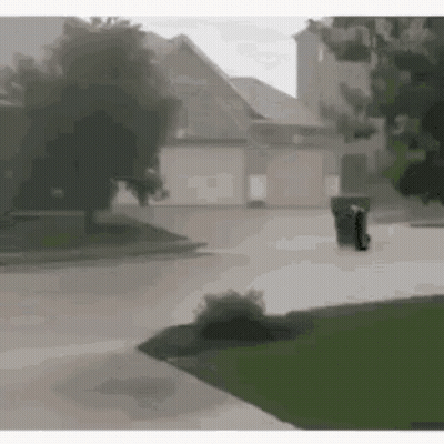 Person Walking Down Sidewalk In Front Of House With Trash Can GIF