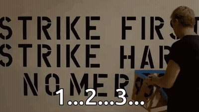 Person Working On Wall Saying Strike First Strike Hard No Mercy GIF