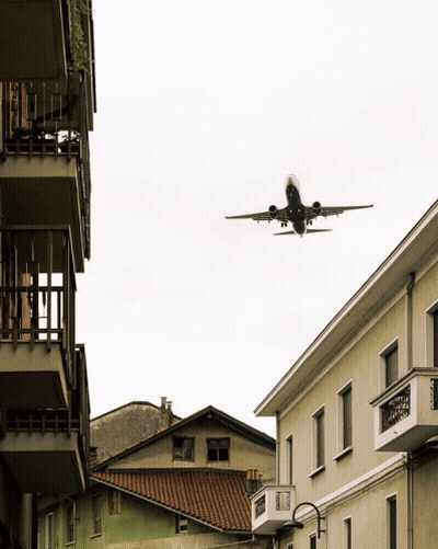 Plane Flying Over Building With Balcony GIF