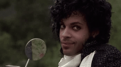 Prince Is Smiling While Sitting On A Motorcycle With A Lollipop In His Hand . GIF