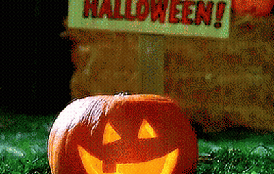 Pumpkin With Carved Face In Front Of Halloween Sign GIF