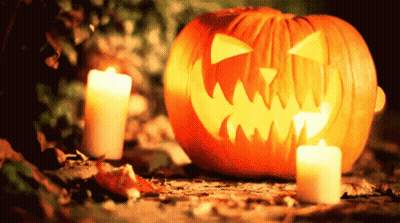 Pumpkin With Carved Face Next To Candles GIF
