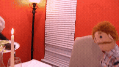 Puppet With Mustache Sitting At Table With Candle GIF