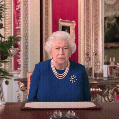 Queen Elizabeth Wearing A Blue Dress And Pearls Sits At A Table GIF
