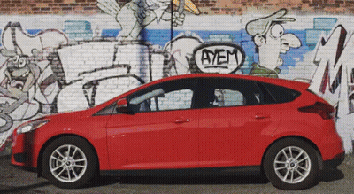 Red Car Parked in Front of Brick Wall With Graffiti Saying Ayem